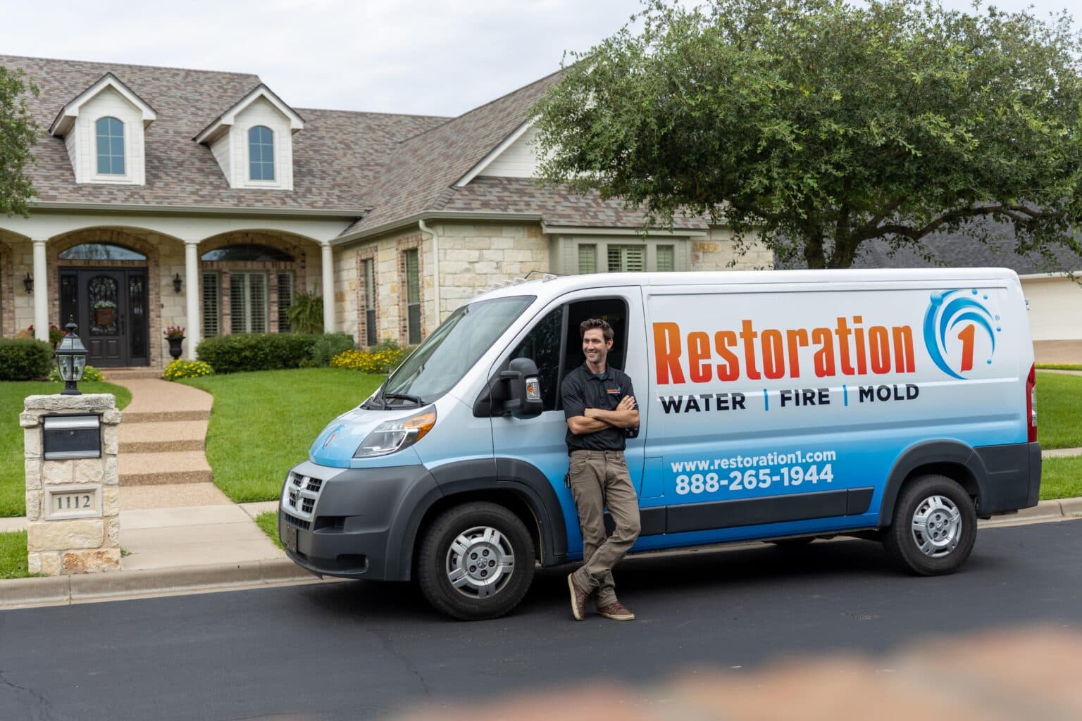 Restoration 1 technician standing beside a branded van outside a restored home